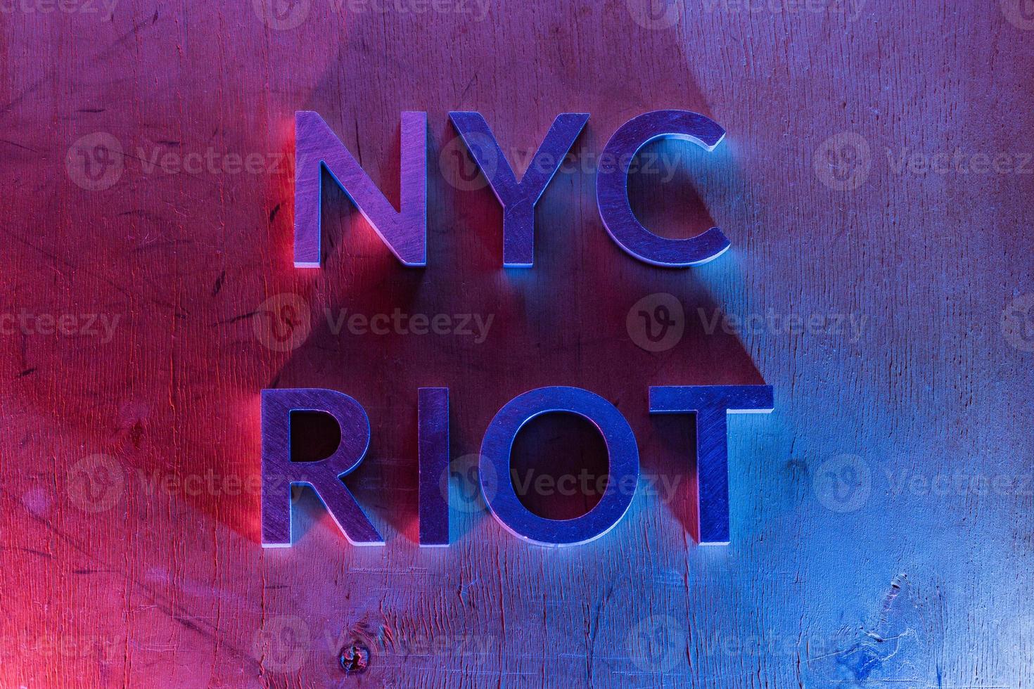 The words NYC riot laid with metal letters on flat plywood surface under red and blue police lights. Concept. photo