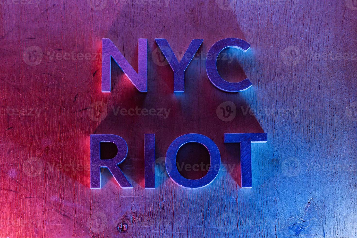 las palabras nyc riot se colocaron con letras de metal sobre una superficie plana de madera contrachapada bajo luces policiales rojas y azules. concepto. foto