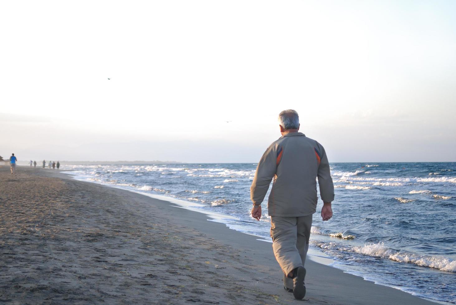lonely older  man walking on beach photo