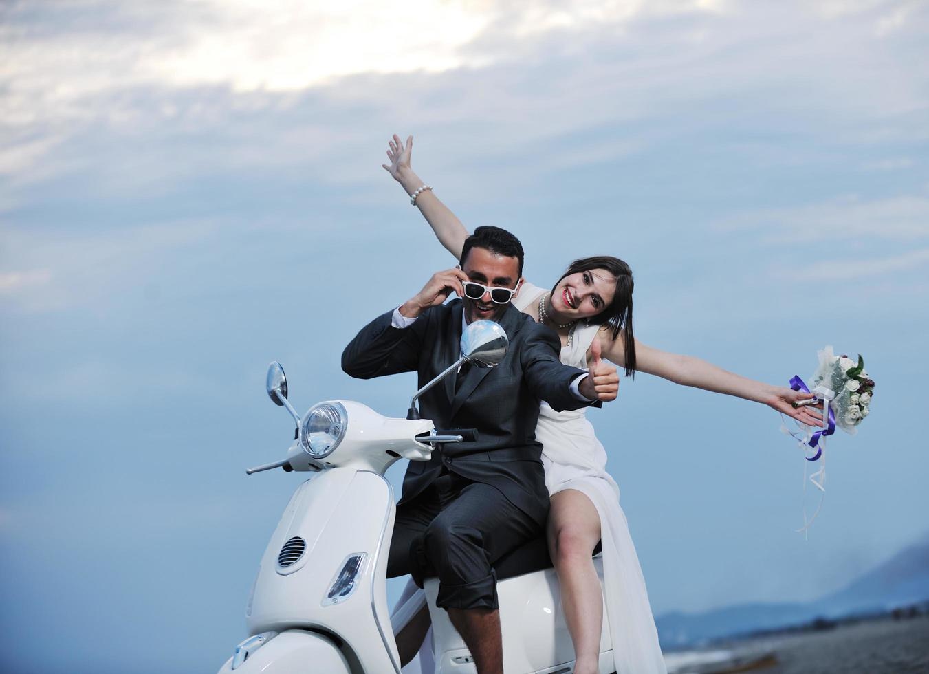 just married couple on the beach ride white scooter photo