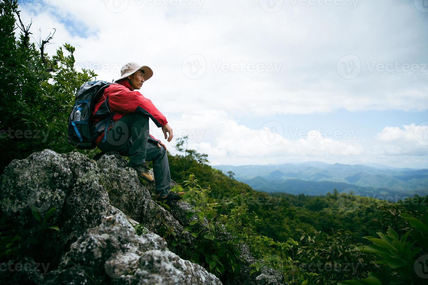 Young person hiking male on top rock, Backpack man looking at beautiful mountain valley at sunlight in summer, Landscape with sport man, high hills, forest, sky. Travel and tourism. photo