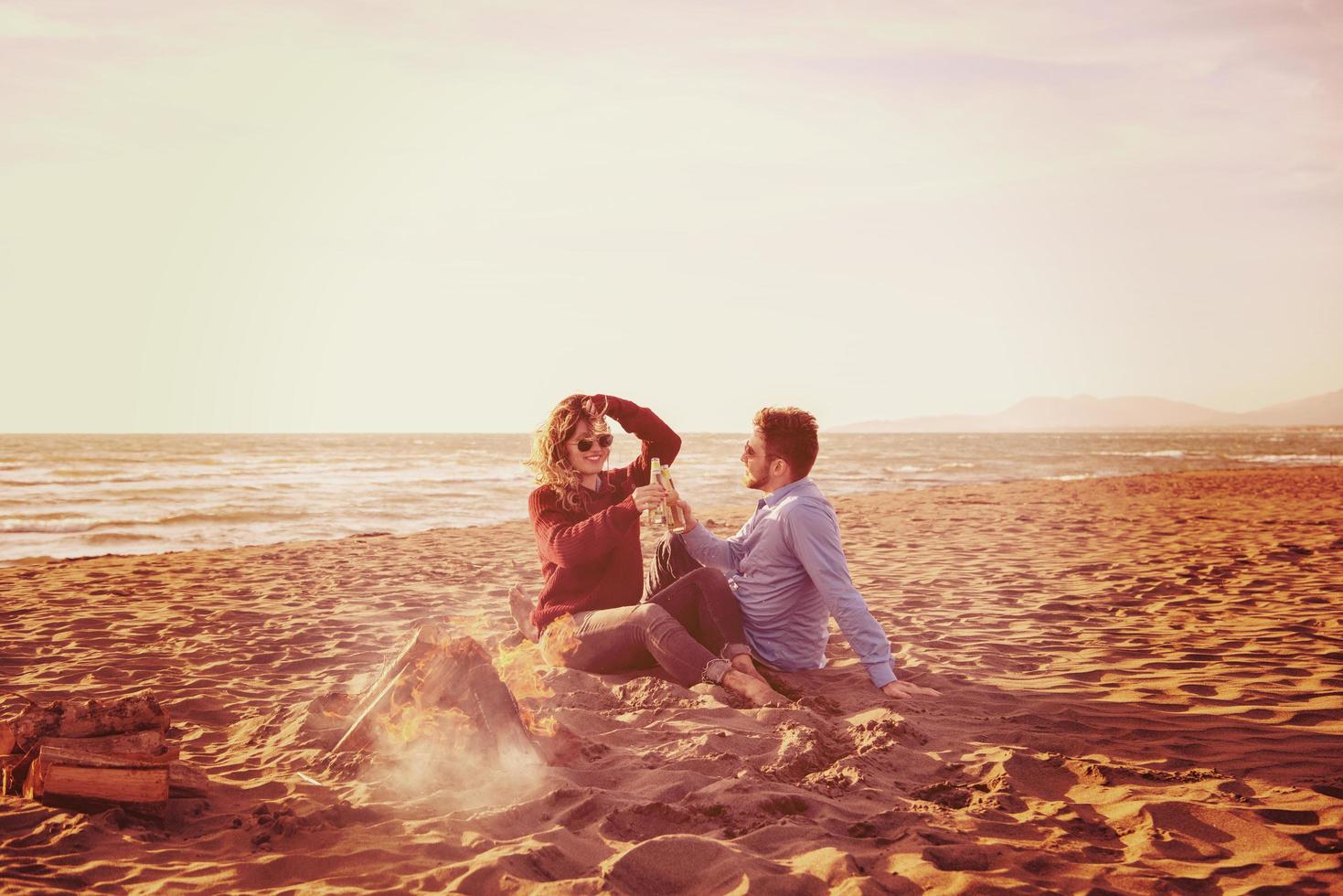 Young Couple Sitting On The Beach beside Campfire drinking beer photo