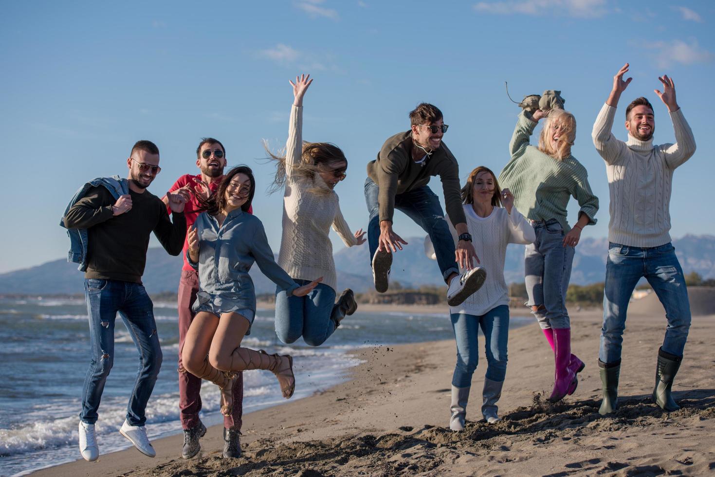 young friends jumping together at autumn beach photo