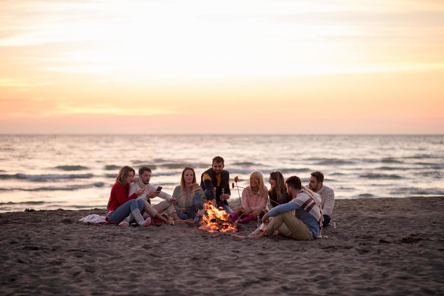 grupo de jóvenes amigos sentados junto al fuego en la playa foto