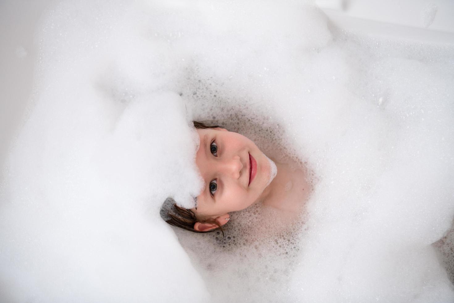 top view of little girl in bath playing with foam photo