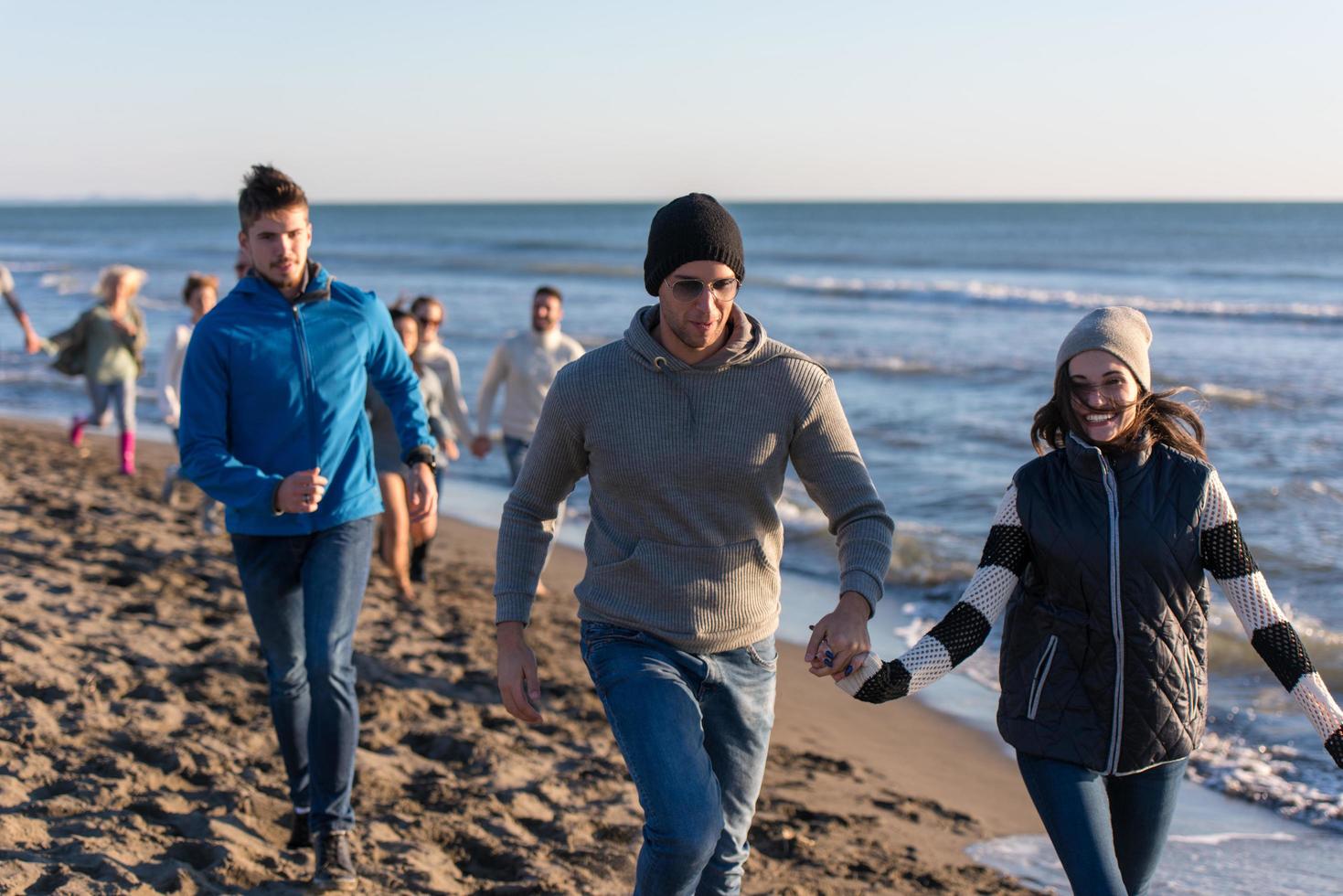 Group of friends running on beach during autumn day photo