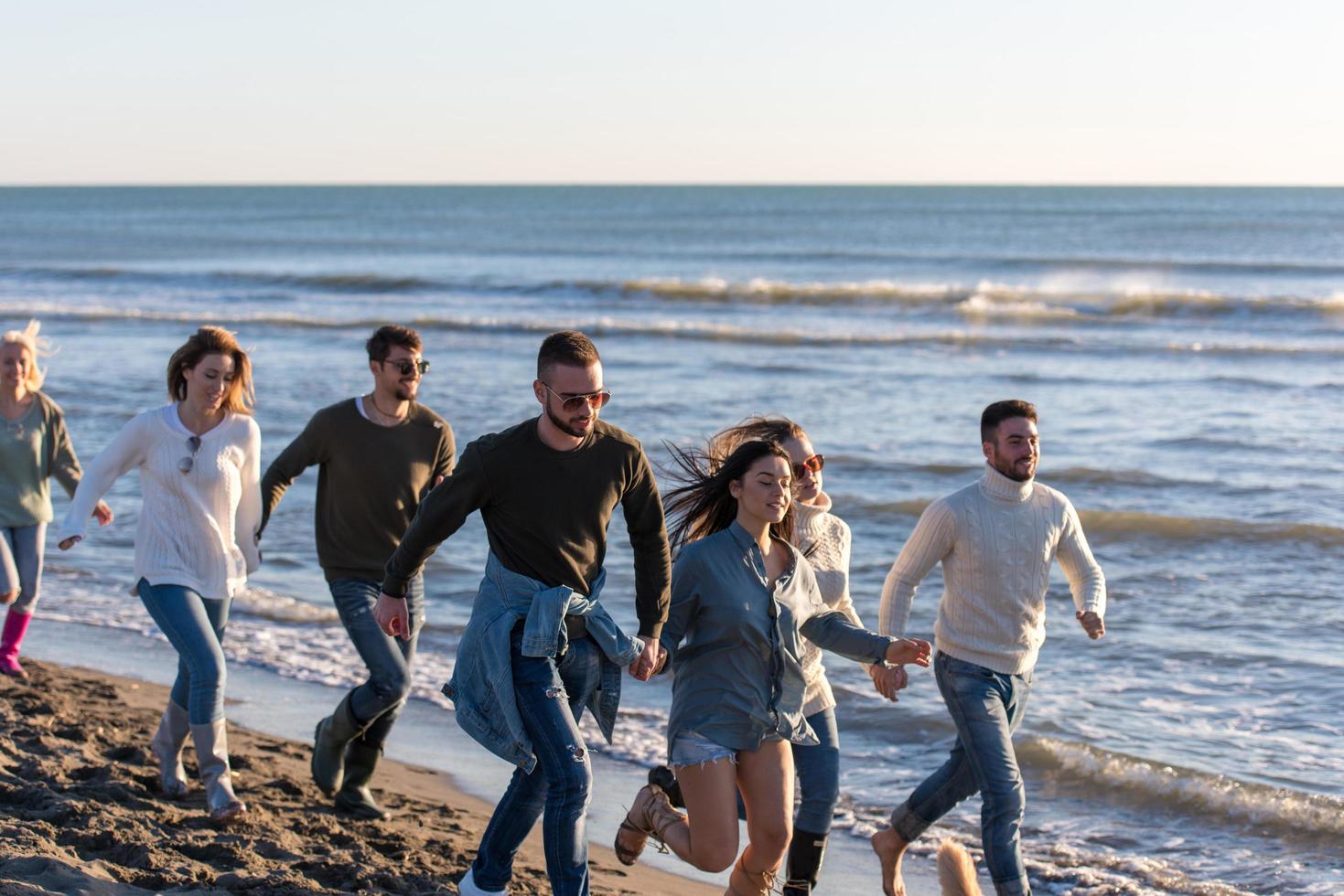 Group of friends running on beach during autumn day photo
