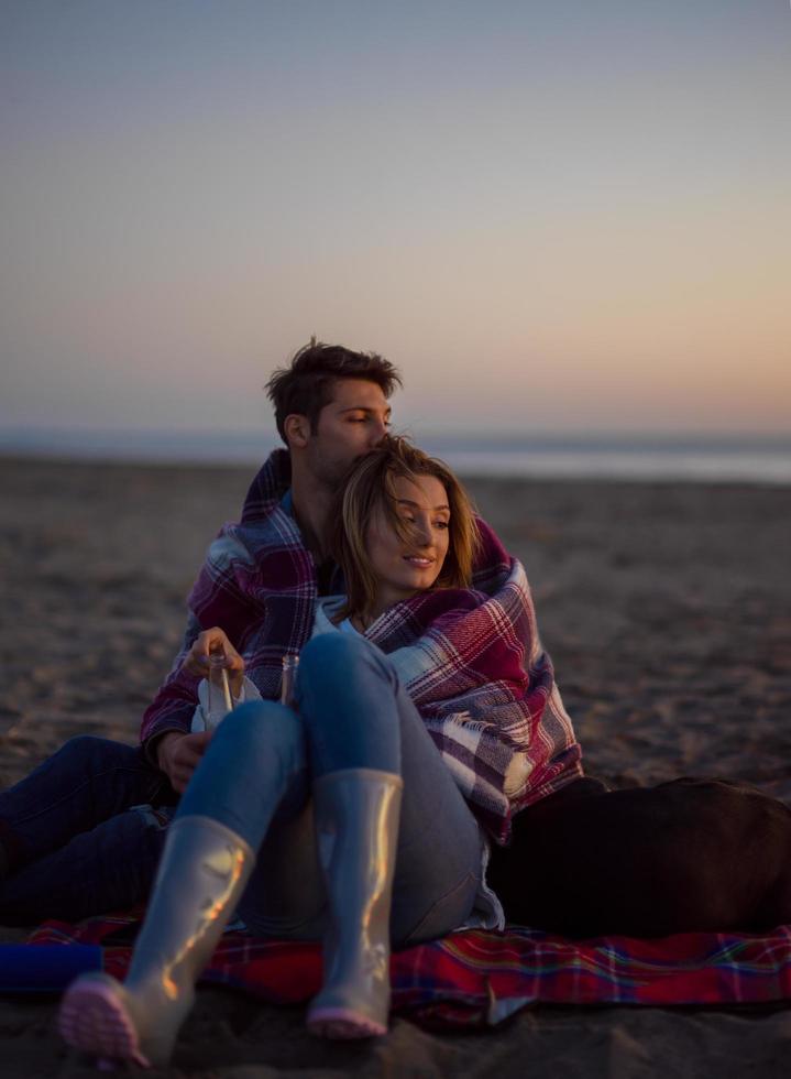 Loving Young Couple Sitting On The Beach beside Campfire drinking beer photo