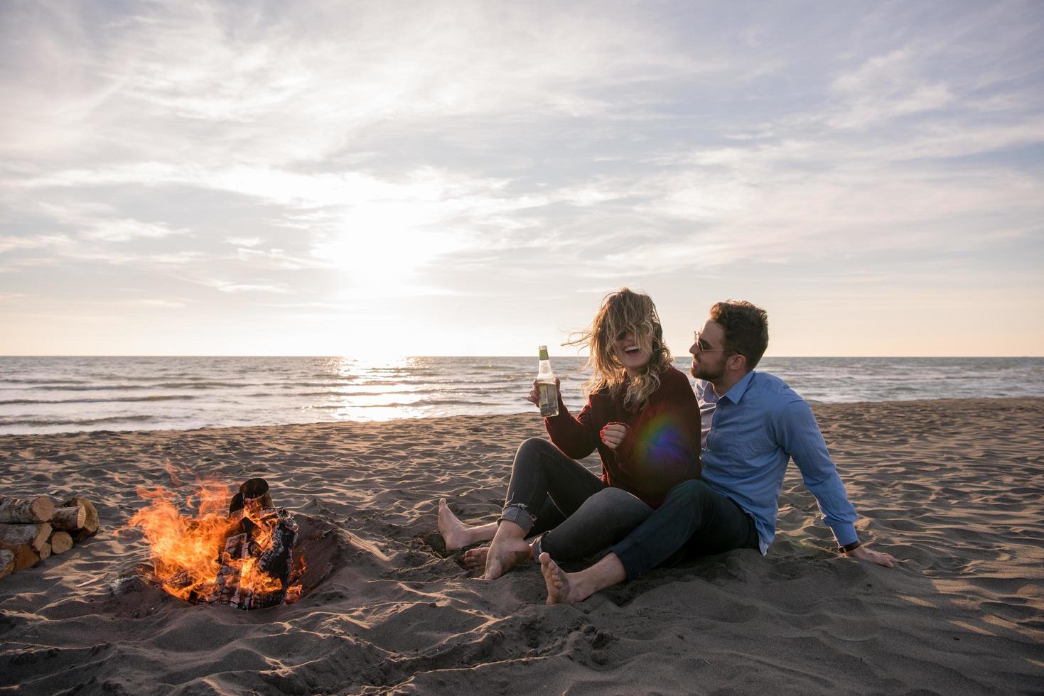 Young Couple Sitting On The Beach beside Campfire drinking beer photo