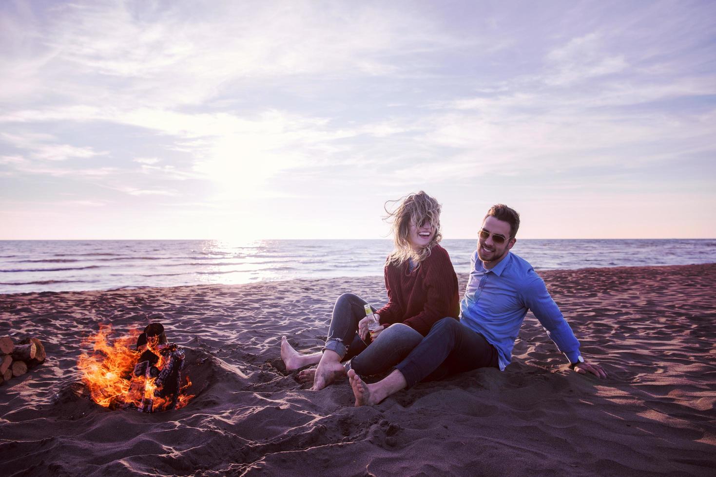 Young Couple Sitting On The Beach beside Campfire drinking beer photo