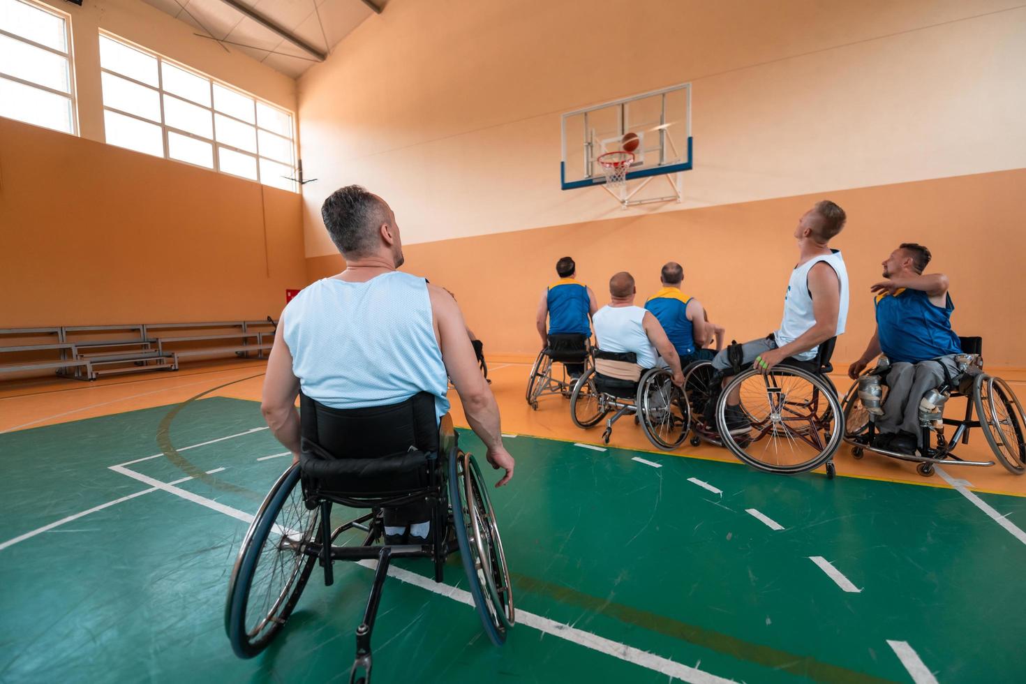 Disabled War veterans mixed race and age basketball teams in wheelchairs playing a training match in a sports gym hall. Handicapped people rehabilitation and inclusion concept photo