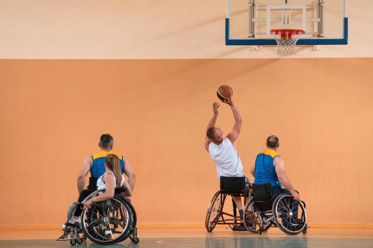 Disabled War veterans mixed race and age basketball teams in wheelchairs playing a training match in a sports gym hall. Handicapped people rehabilitation and inclusion concept photo