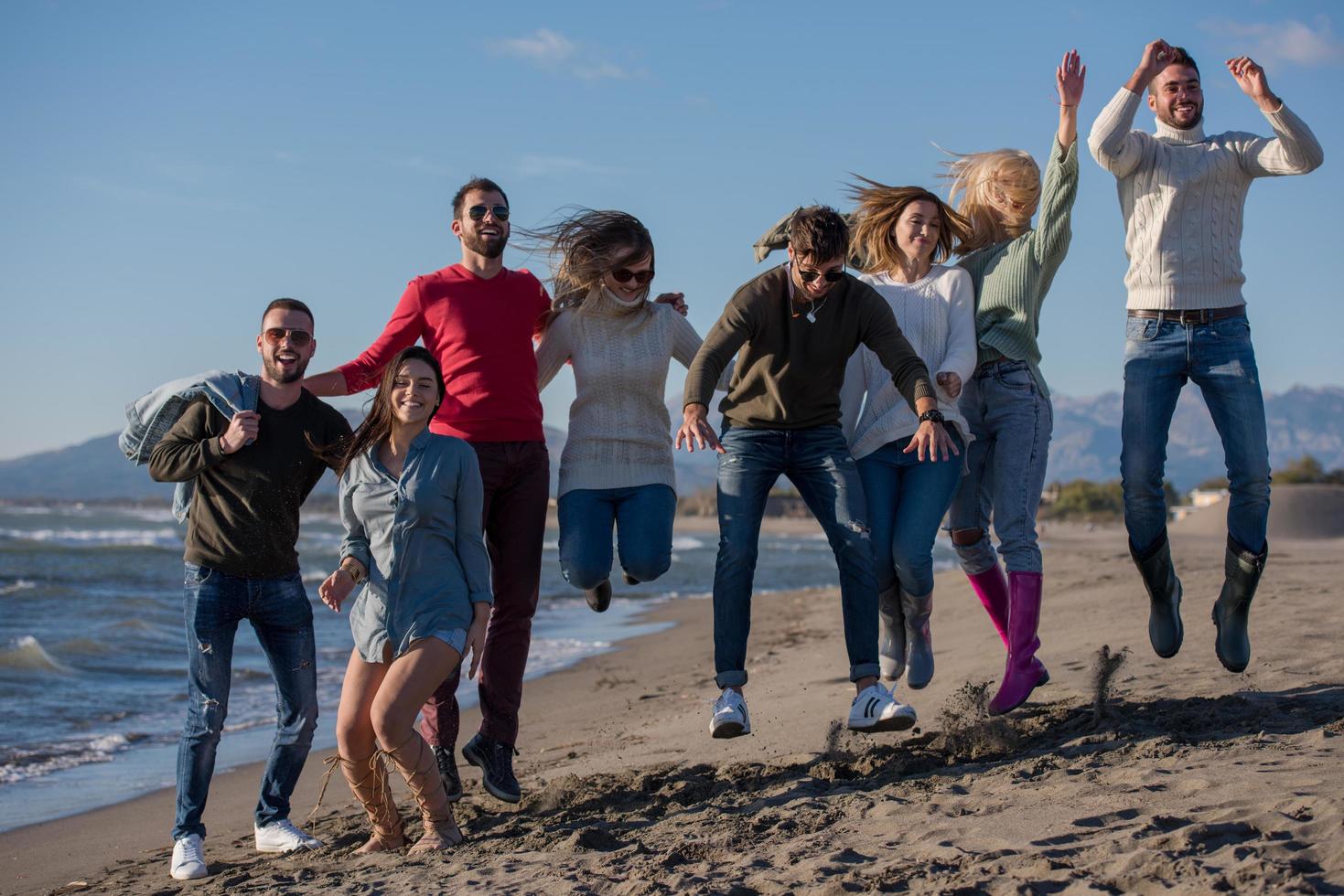 jóvenes amigos saltando juntos en la playa de otoño foto