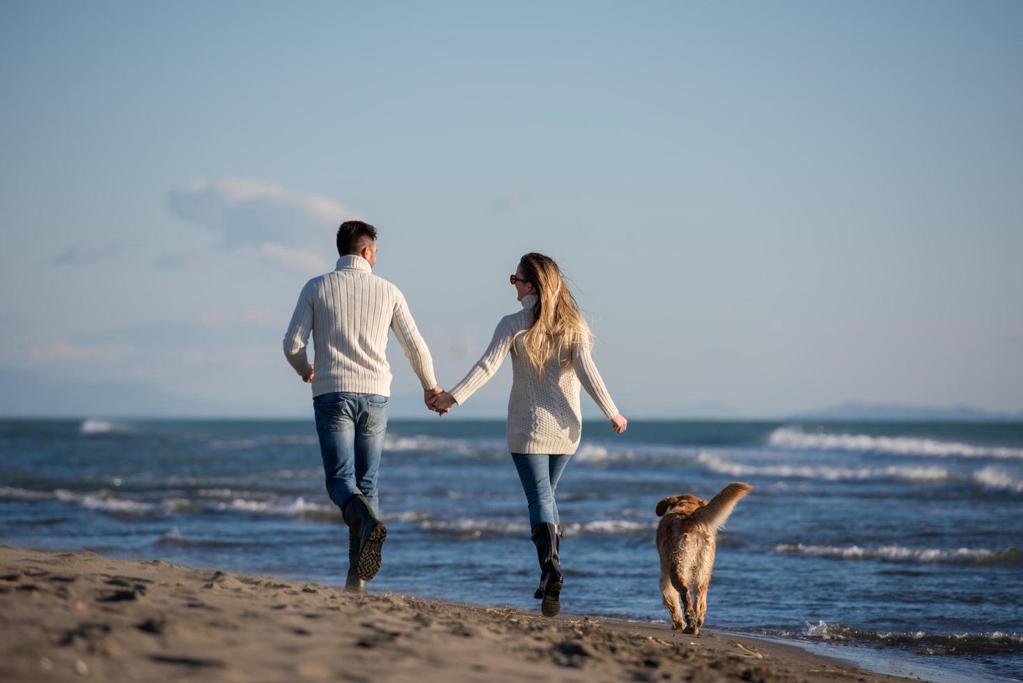 couple with dog having fun on beach on autmun day photo