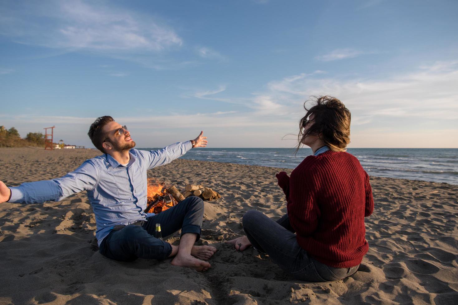 Young Couple Sitting On The Beach beside Campfire drinking beer photo