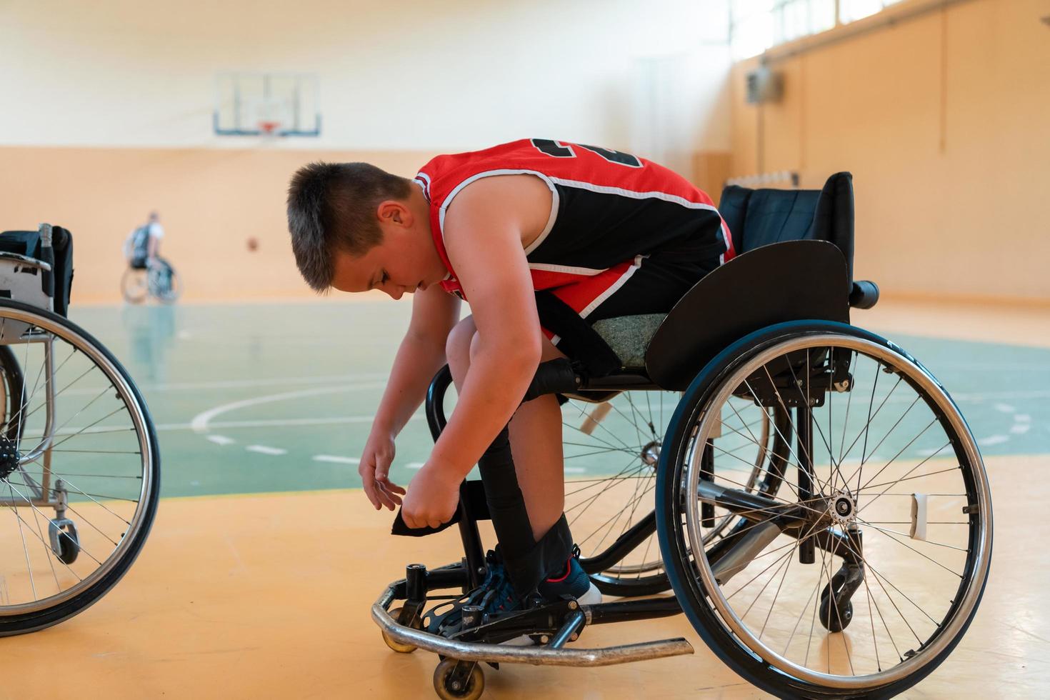 el niño se sienta en una silla de ruedas y se prepara para el comienzo del juego de baloncesto en la gran arena foto