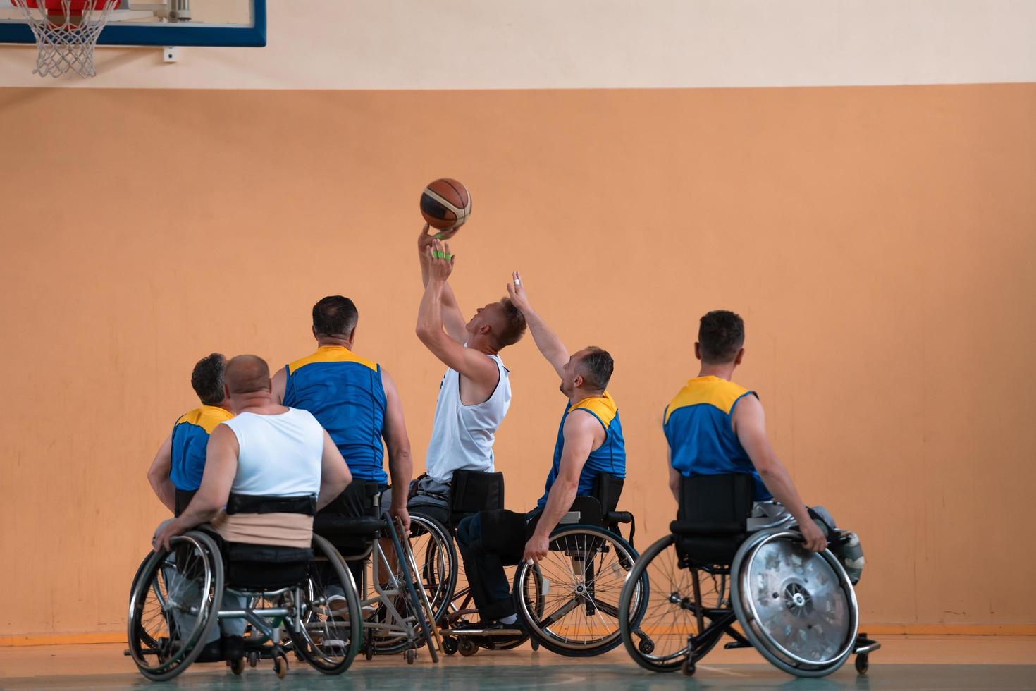 Disabled War veterans mixed race and age basketball teams in wheelchairs playing a training match in a sports gym hall. Handicapped people rehabilitation and inclusion concept photo