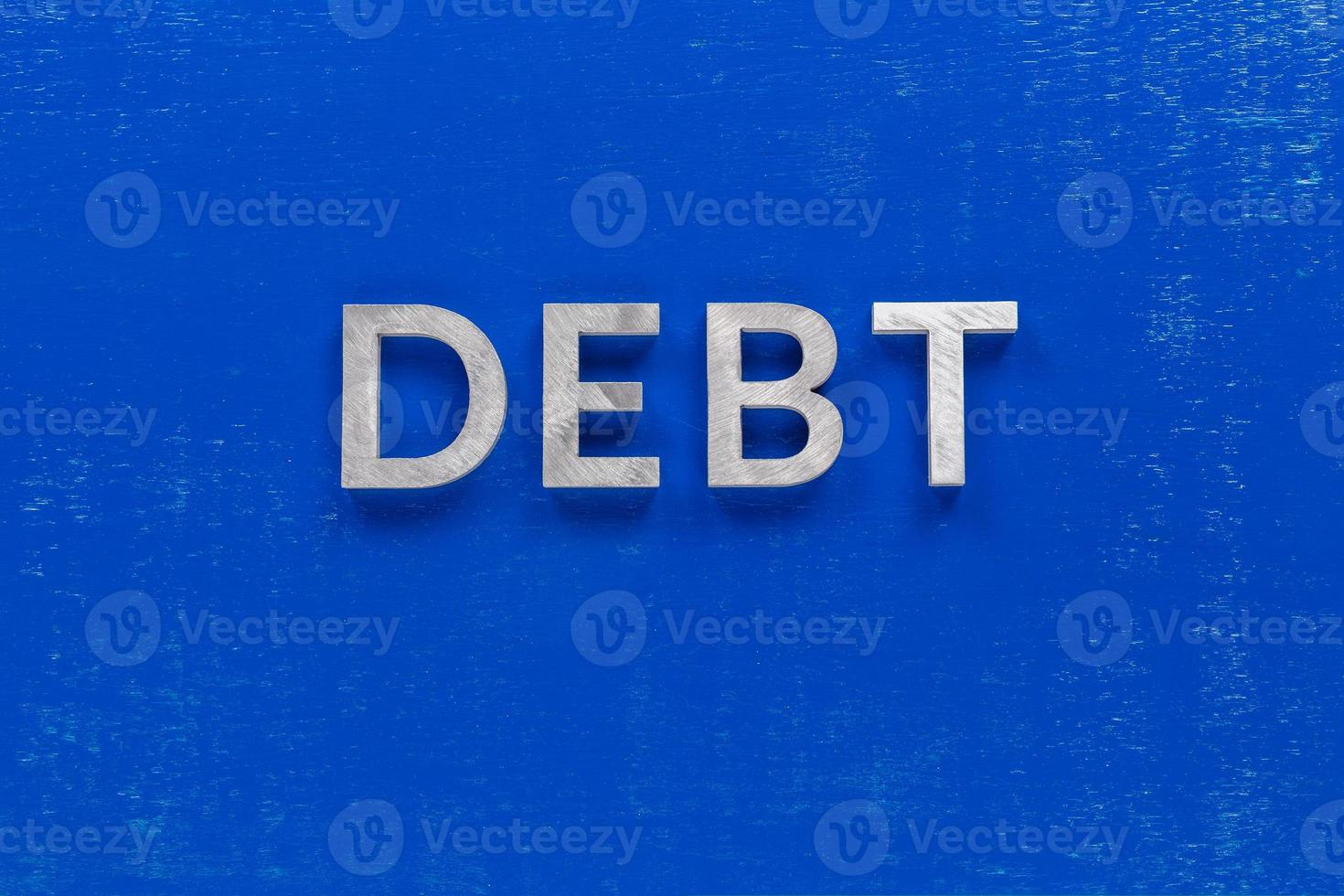 la palabra deuda colocada en una tabla pintada de azul con gruesos caracteres alfabéticos de metal plateado foto