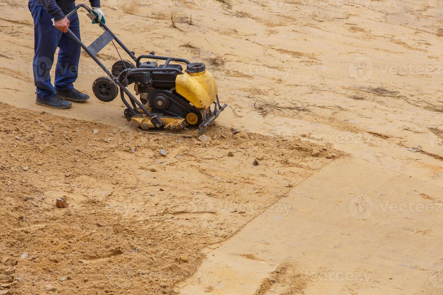 Worker in use vibratory plate compactor for path construction. Plate compactor for compaction sand. photo