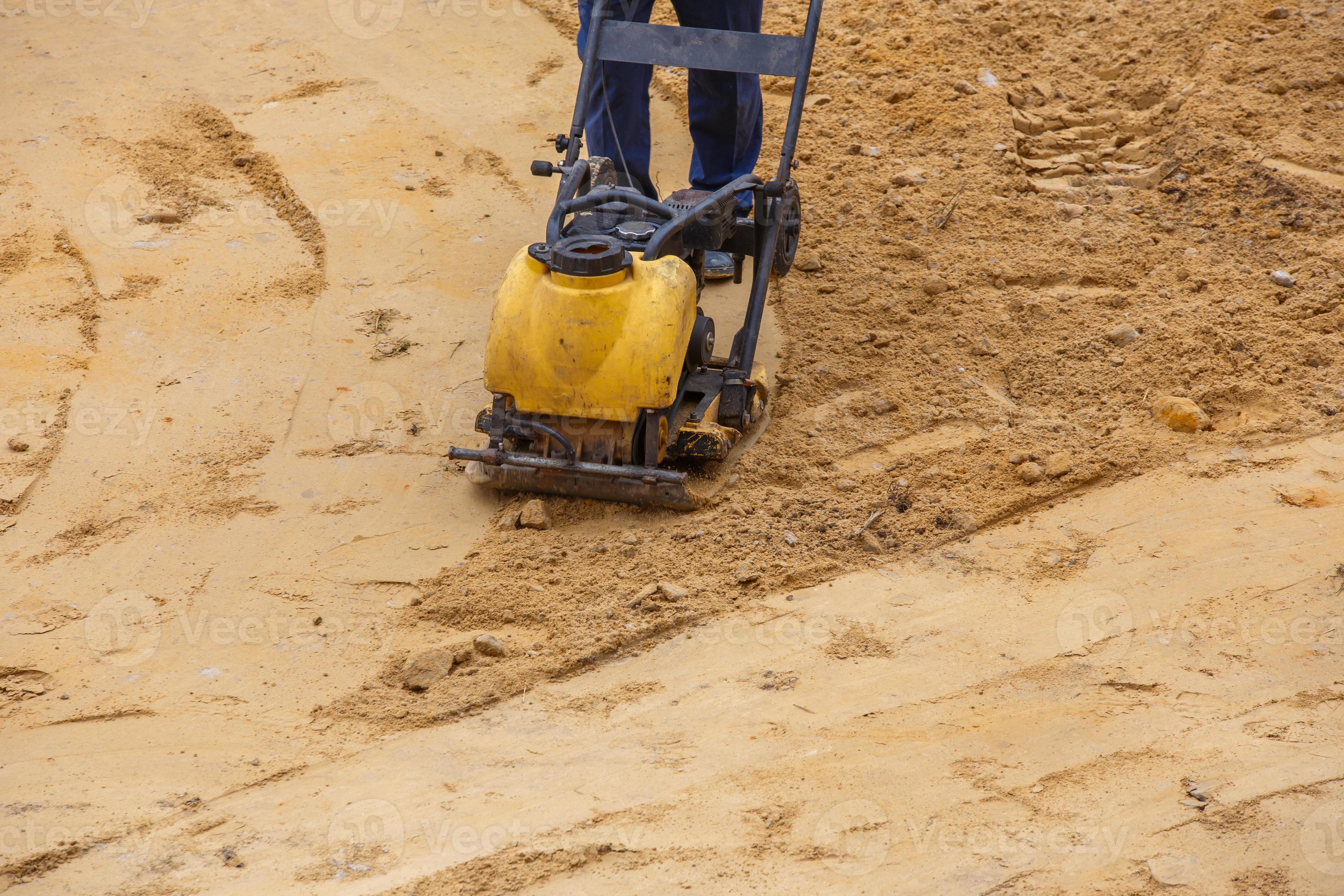 Worker in use vibratory plate compactor for path construction. Plate
