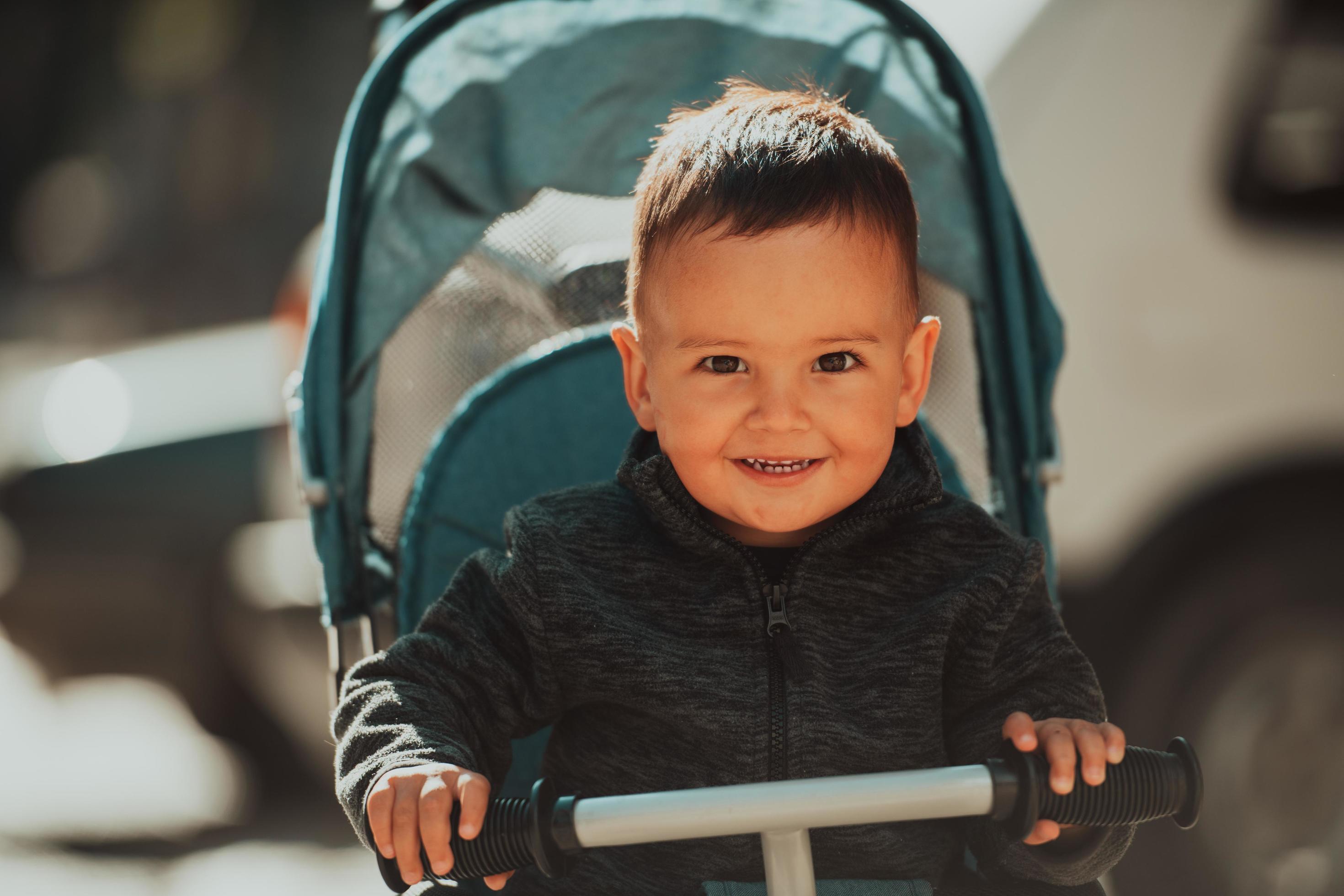 Sweet baby boy in a stroller bicycle outdoors. Little child in a pram