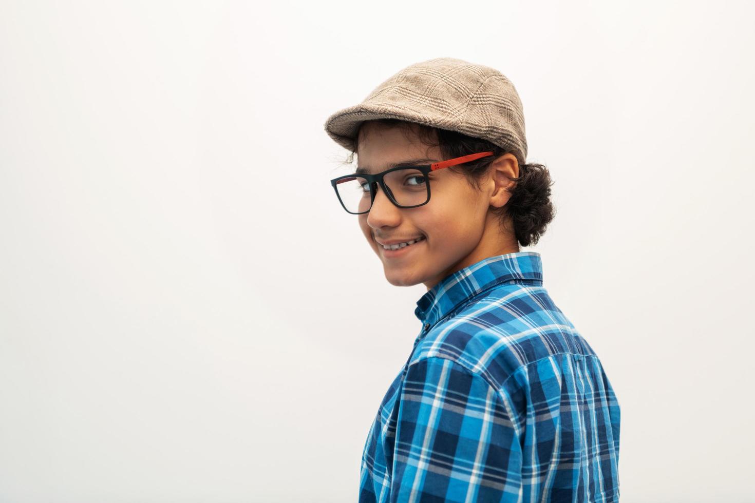 retrato de un adolescente árabe de aspecto inteligente con gafas que lleva un sombrero en un aspecto informal de la escuela aislado en un espacio de copia en blanco foto