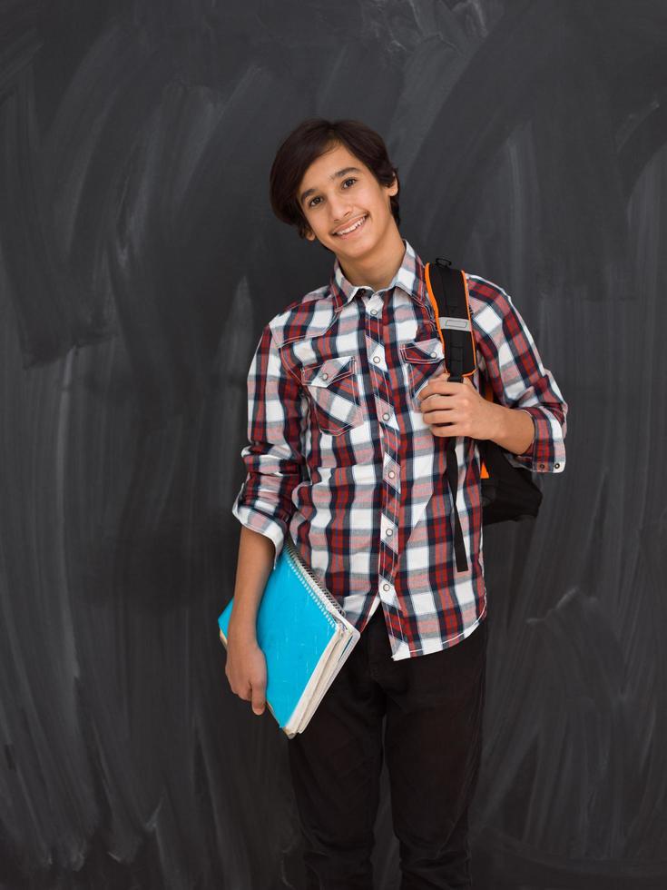 arab teenager with backpack wearing casual school look against black chalkboard background photo