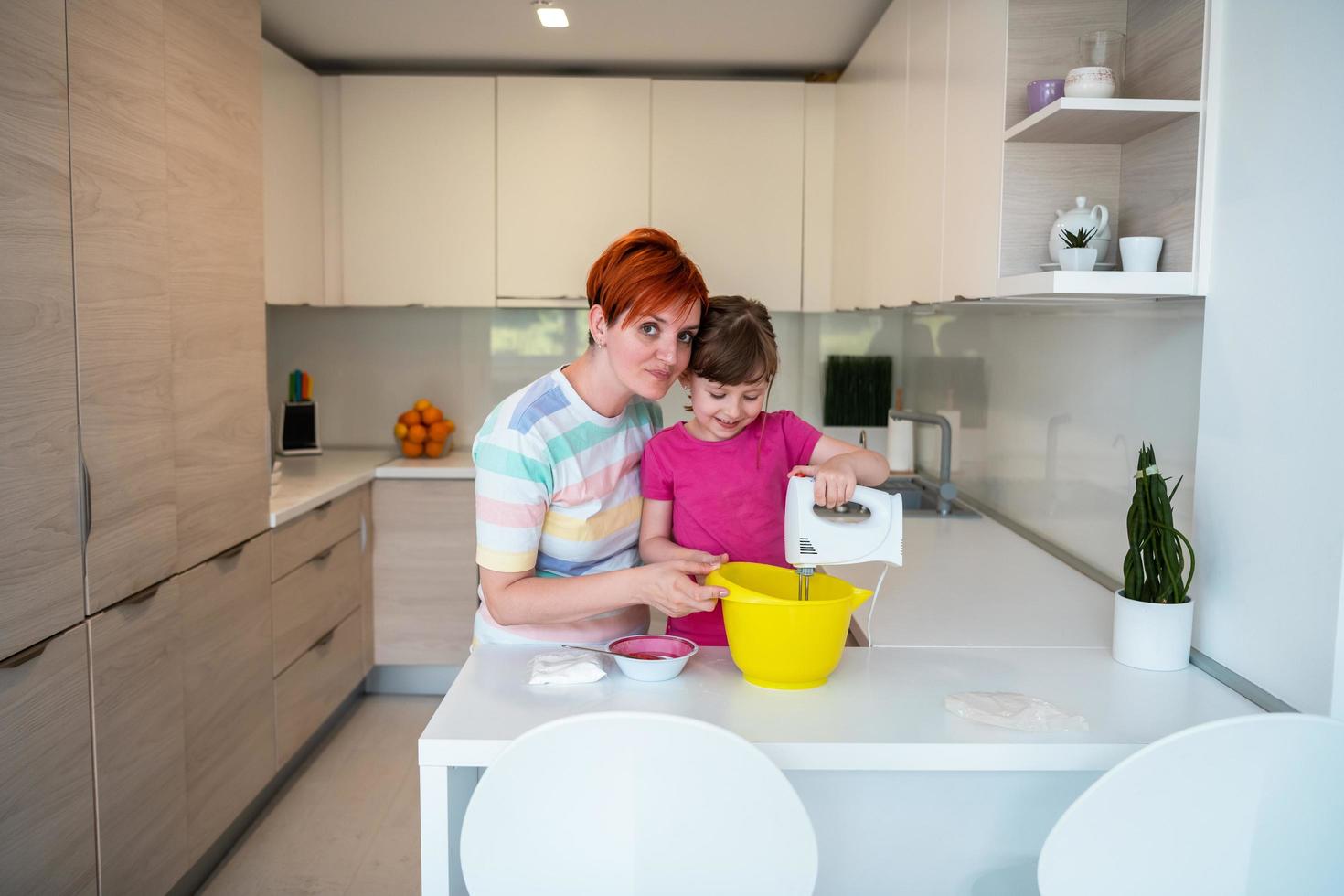 Funny little girl helper playing with dough on his hands learning to knead helps adult mom in the kitchen, happy cute baby daughter and parent mom have fun cooking cookies. photo