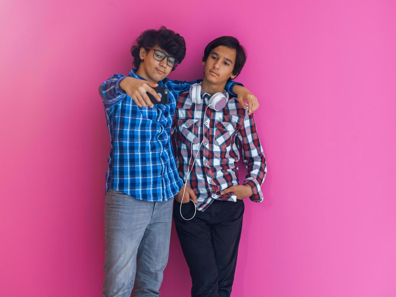 Photo of a young arab teenager taking a selfie photo with a smartphone isolated behind a purple wall. Selective focus