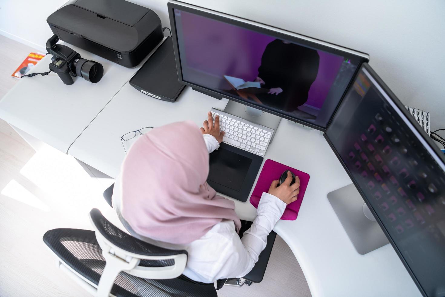 Female Arabic creative professional working at home office on desktop computer with dual screen monitor top view. Selectve focus photo