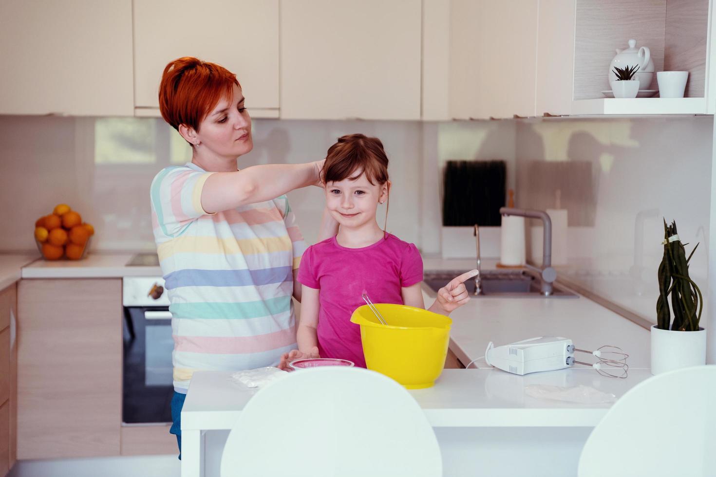 Funny little girl helper playing with dough on his hands learning to knead helps adult mom in the kitchen, happy cute baby daughter and parent mom have fun cooking cookies. photo