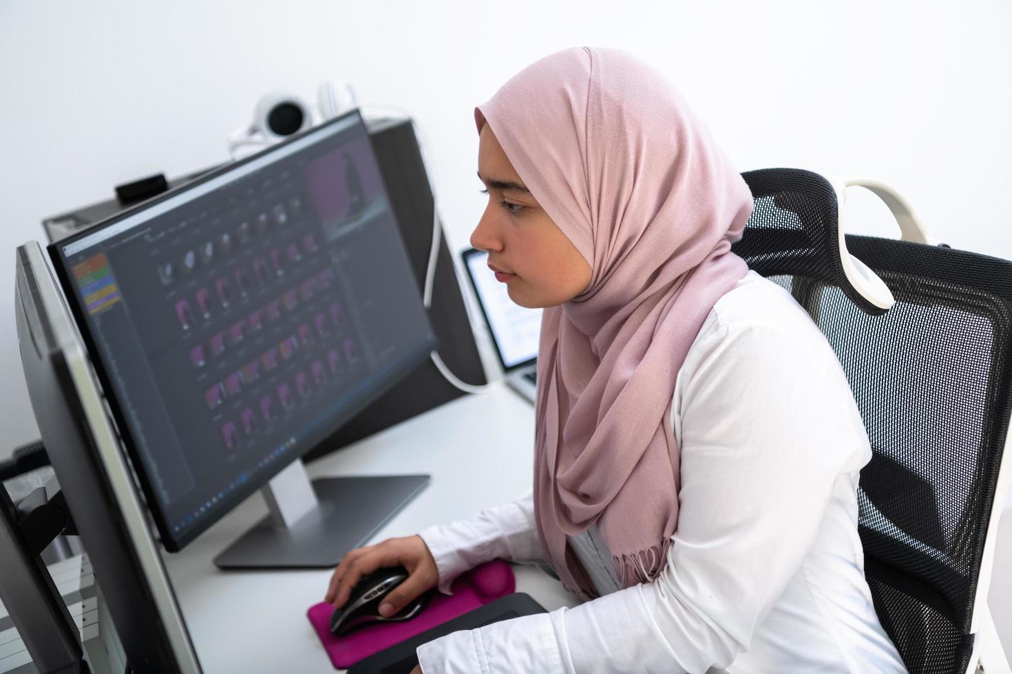 Female Arabic creative professional working at home office on desktop computer with dual screen monitor top view. Selectve focus photo