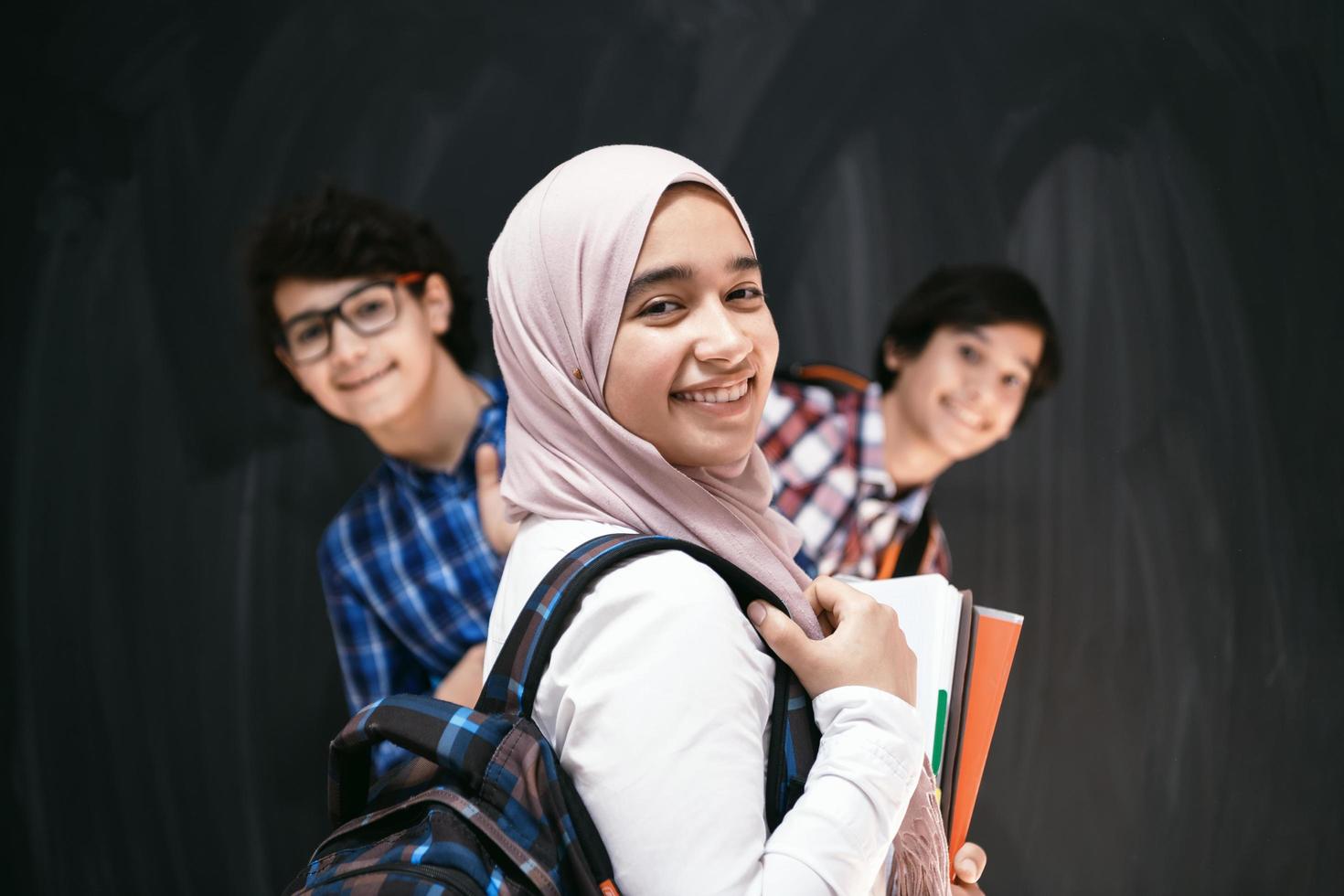 adolescentes árabes, retrato de grupo de estudiantes contra pizarra negra con mochila y libros en la escuela. enfoque selectivo foto