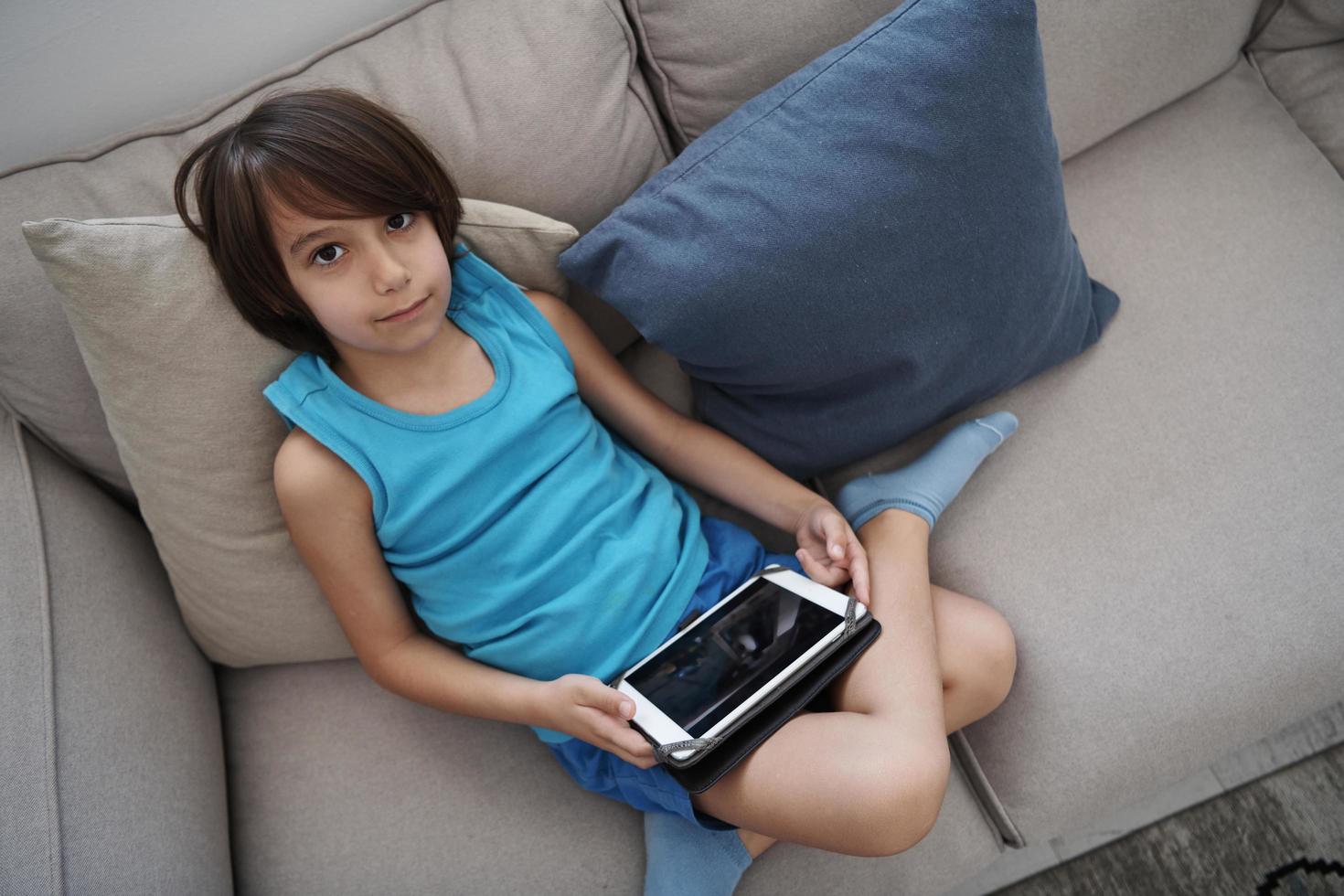 Little Arabian boy sitting on sofa and playing game on digital tablet photo