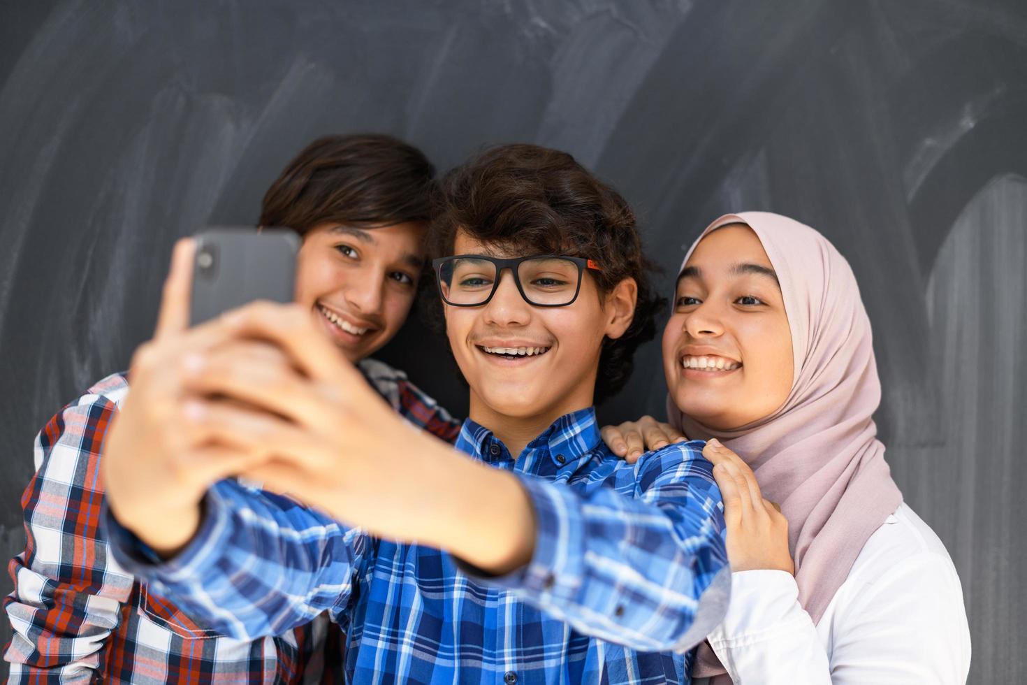 grupo de adolescentes árabes tomando una foto selfie en un teléfono inteligente con pizarra negra en el fondo. enfoque selectivo