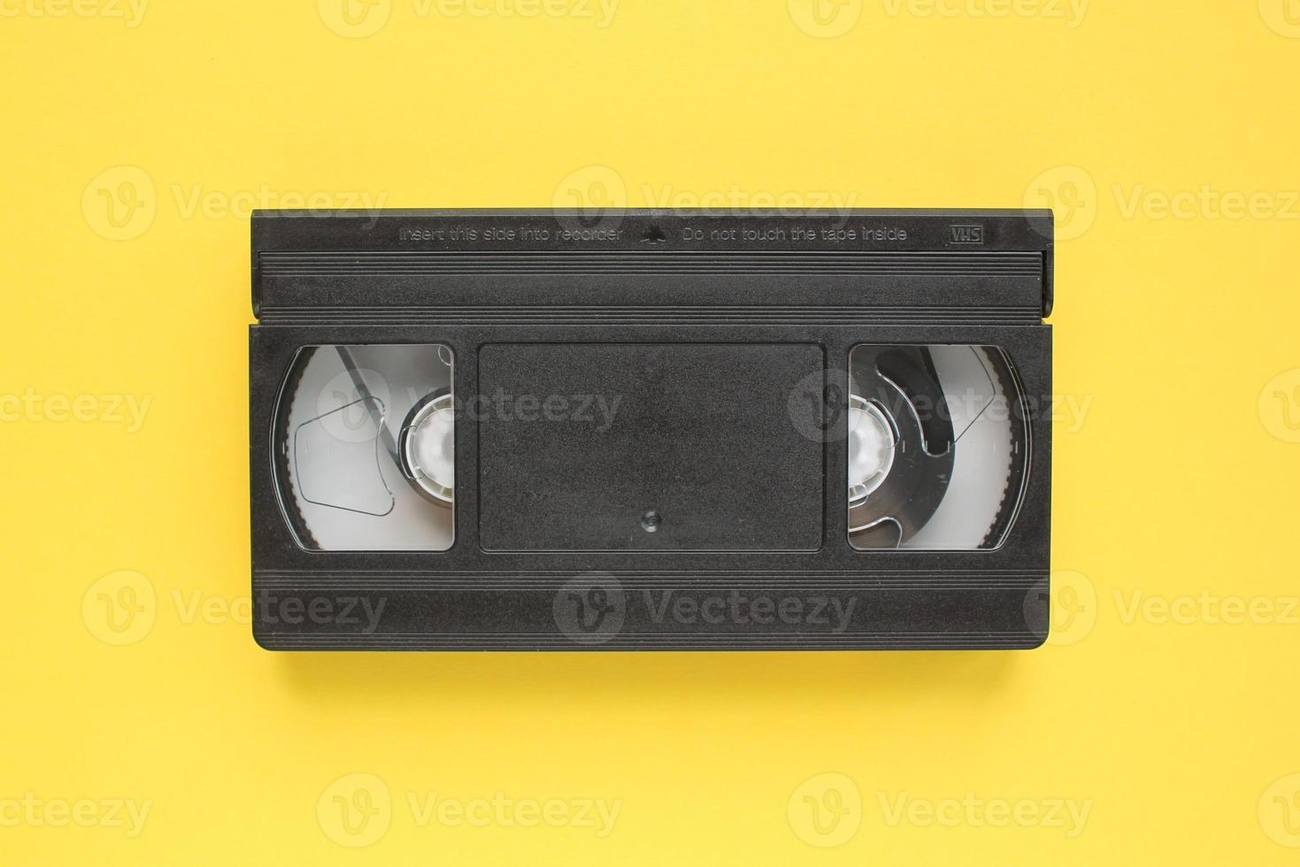 Black VHS videotape recorder cassette on yellow background. Old obsolete technology for tape recording and watching media movies. Retro, vintage, history, nostalgia concept. Top view, flat lay photo