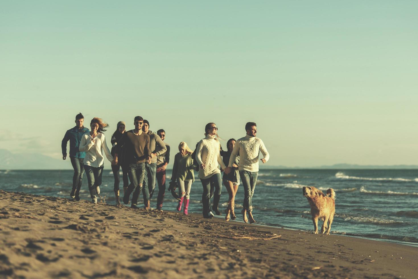 Group of friends running on beach during autumn day photo