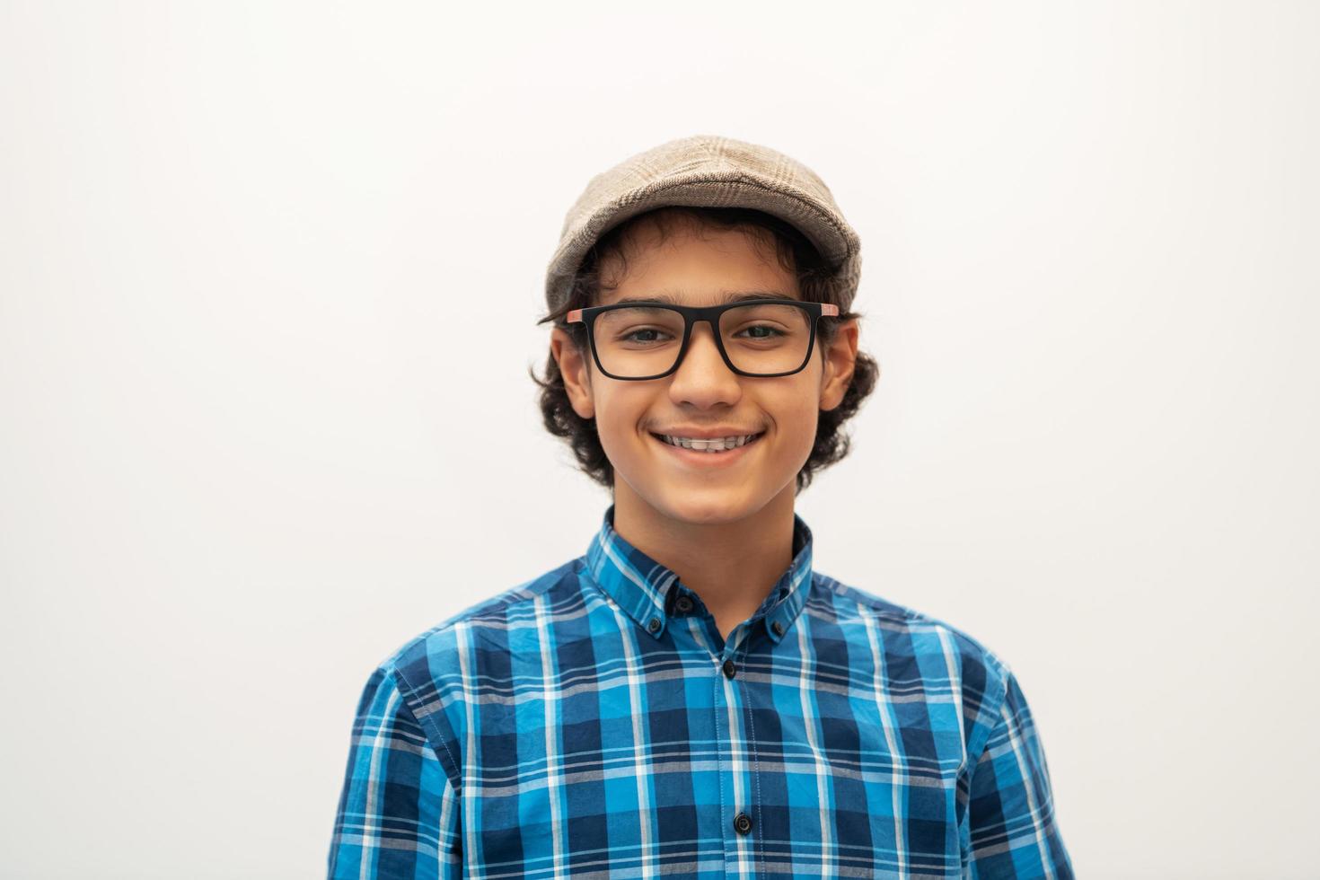 retrato de un adolescente árabe de aspecto inteligente con gafas que lleva un sombrero en un aspecto informal de la escuela aislado en un espacio de copia en blanco foto