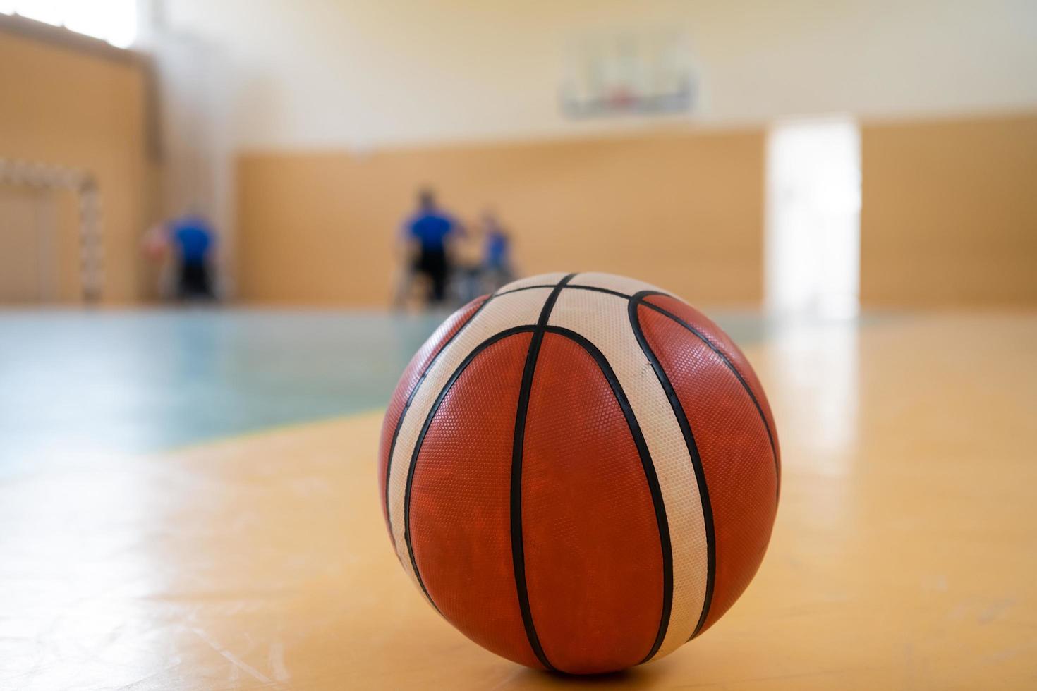 foto de cerca de una pelota de baloncesto en la cancha, en el fondo un equipo deportivo de personas con discapacidad preparándose para un juego