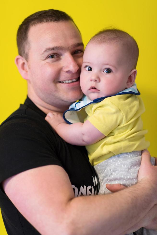 retrato de un joven padre feliz sosteniendo a un bebé aislado en amarillo foto