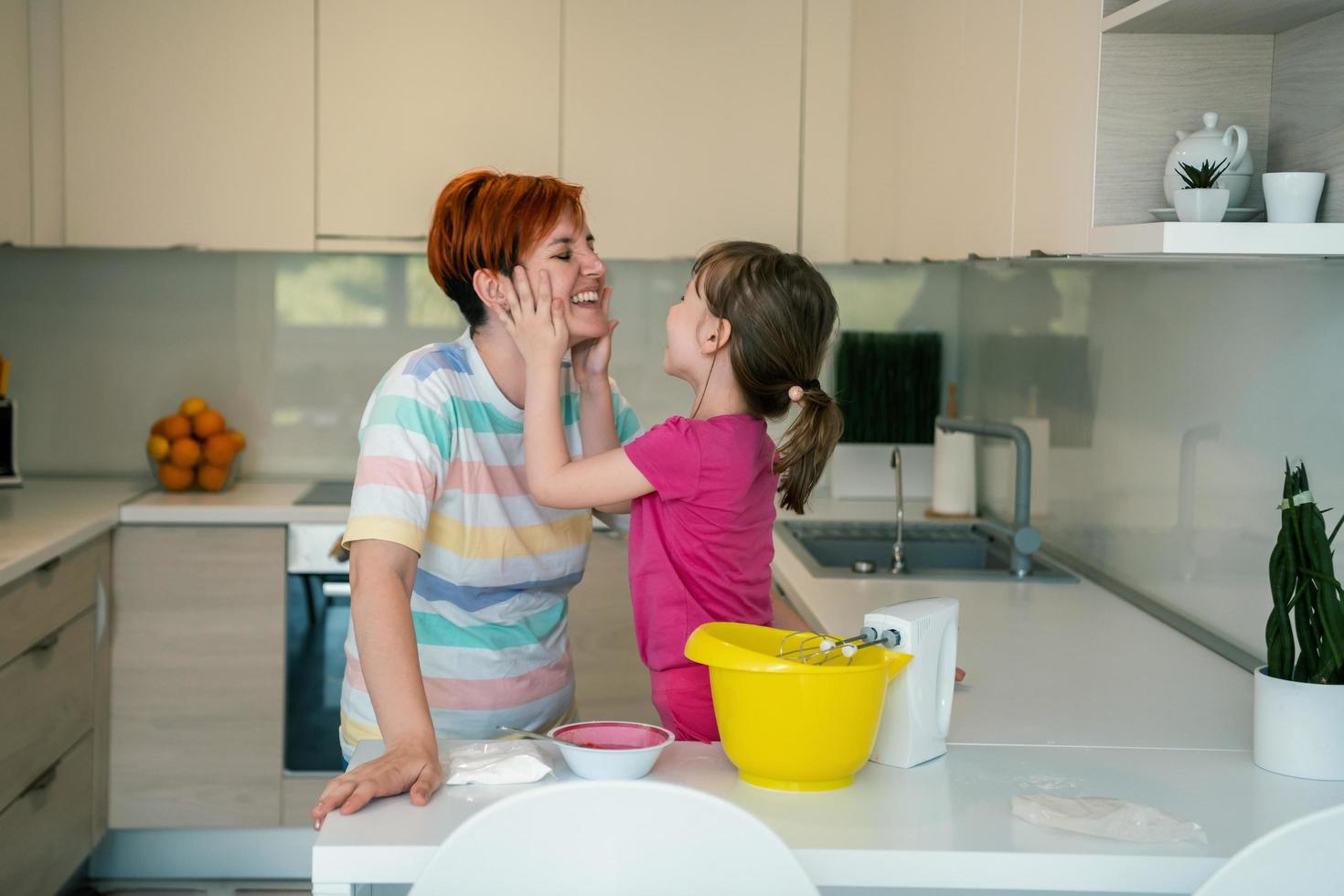 una niñita divertida que juega con masa en las manos aprendiendo a amasar ayuda a la madre adulta en la cocina, la feliz y linda hija y la madre se divierten cocinando galletas. foto