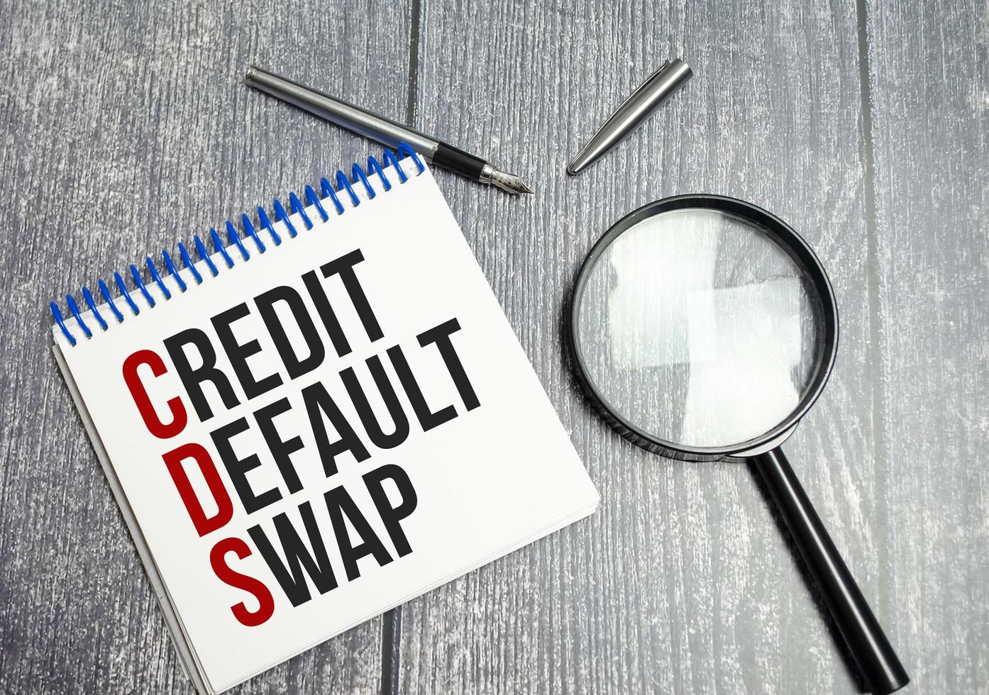 CDS Credit Default Swap text on white paper on wooden background and magnifier photo