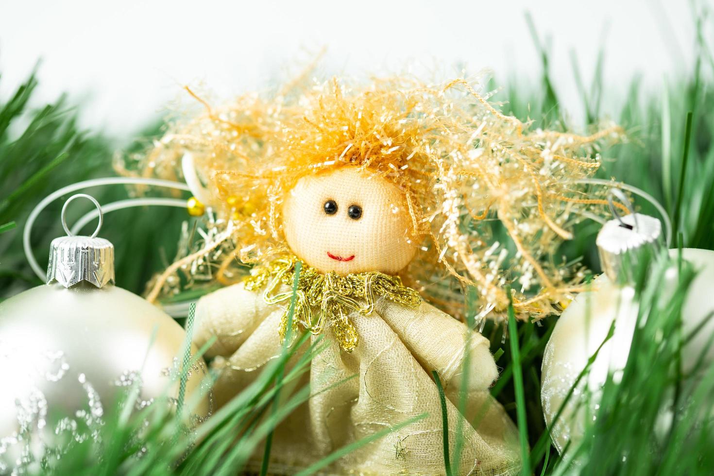 un ángel entre bolas de navidad plateadas y ramas de árboles de navidad. Adorno navideño de tela hecho a mano. foto