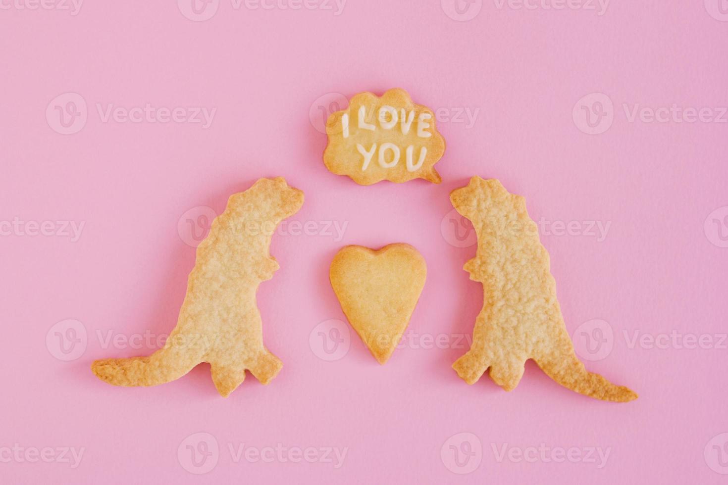 Homemade shortbread cookies with white glaze on pink background, top view. Two dinosaurs with callout cloud with text - I love you photo