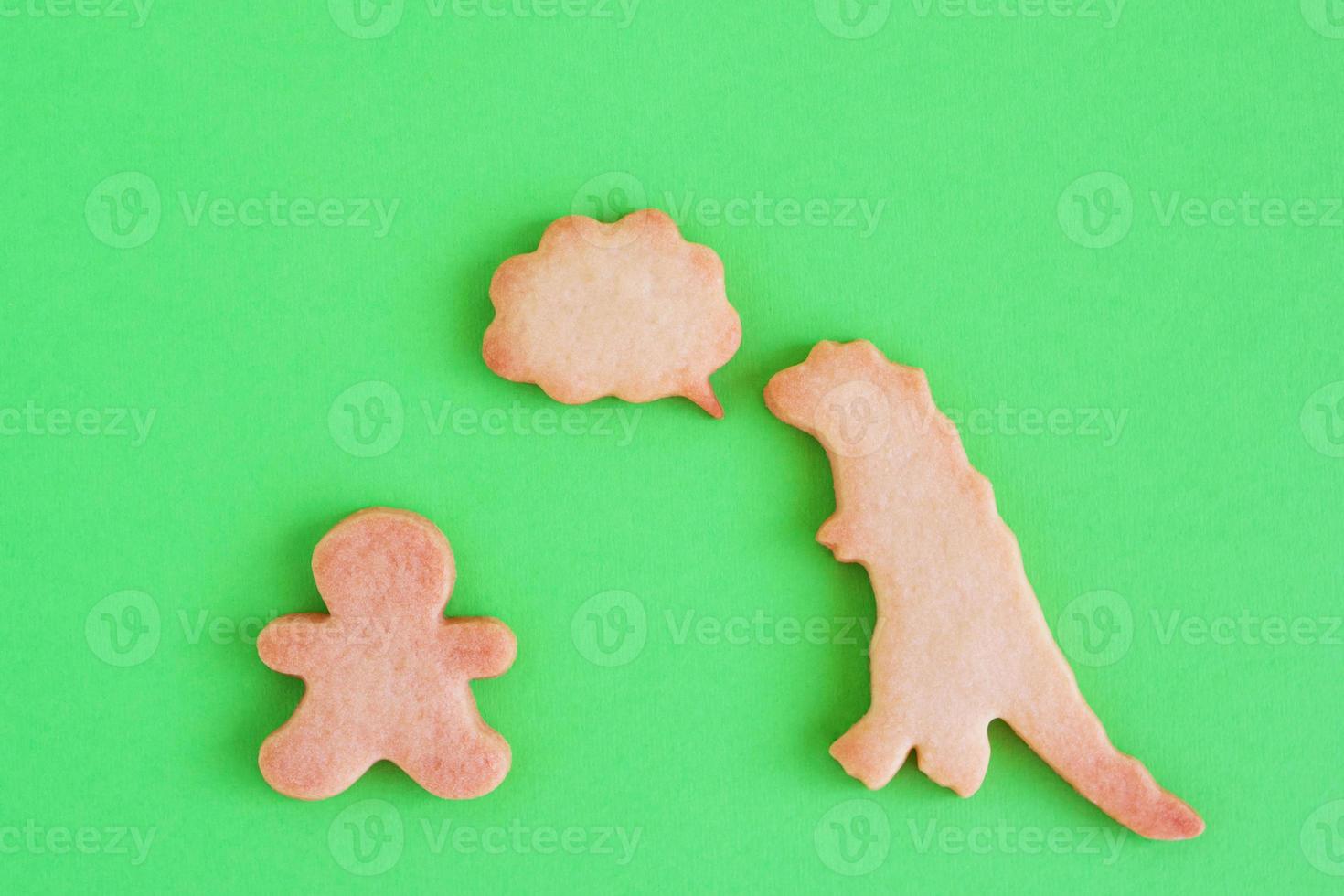 Homemade shortbread cookies in shapes of dinosaur and man with callout cloud on green background, top view. photo