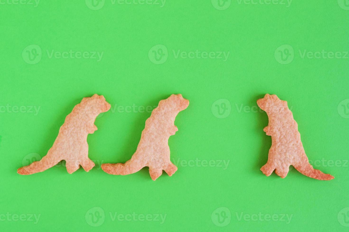 Homemade cookies in shapes of dinosaurs on green background, top view. Sweet shortbread with white glaze. Social distancing concept. photo