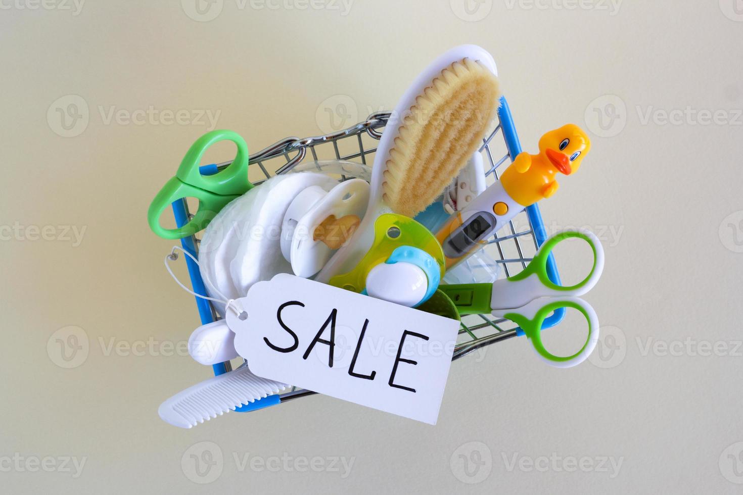 Flat lay on shopping basket with baby care items - scissors, hairbrushes, pacifiers, thermometer, cotton pads, pacifier holders and nasal aspirator - on a beige background with paper price tag. photo