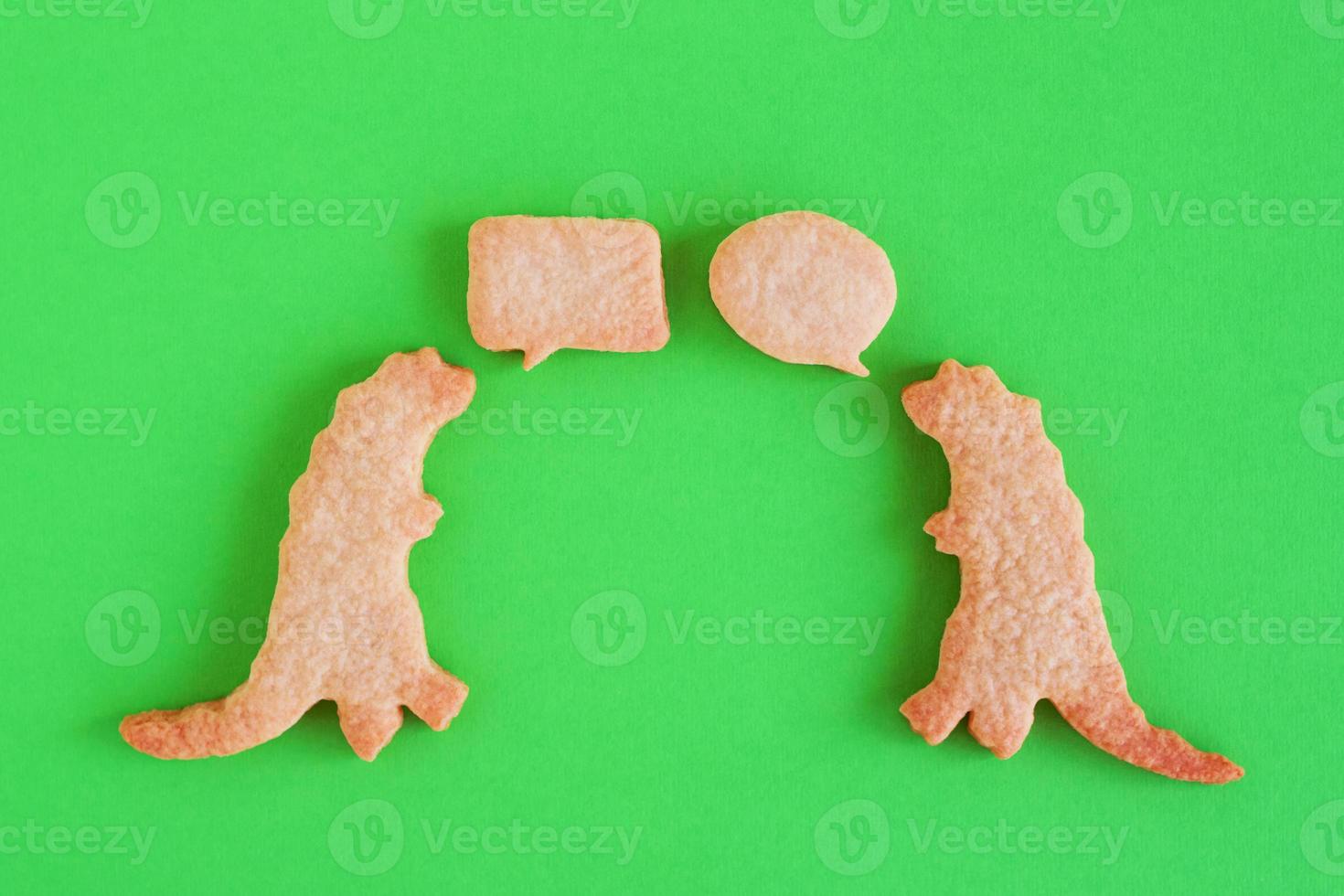 Homemade shortbread cookies in shapes of dinosaurs with callout clouds on green background, top view. photo