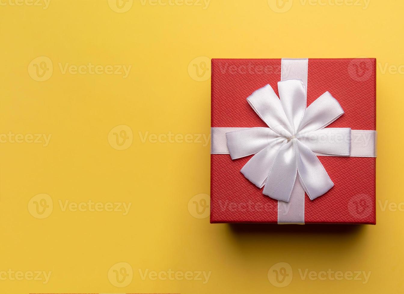 Red gift box with white bow on yellow background,flat lay photo