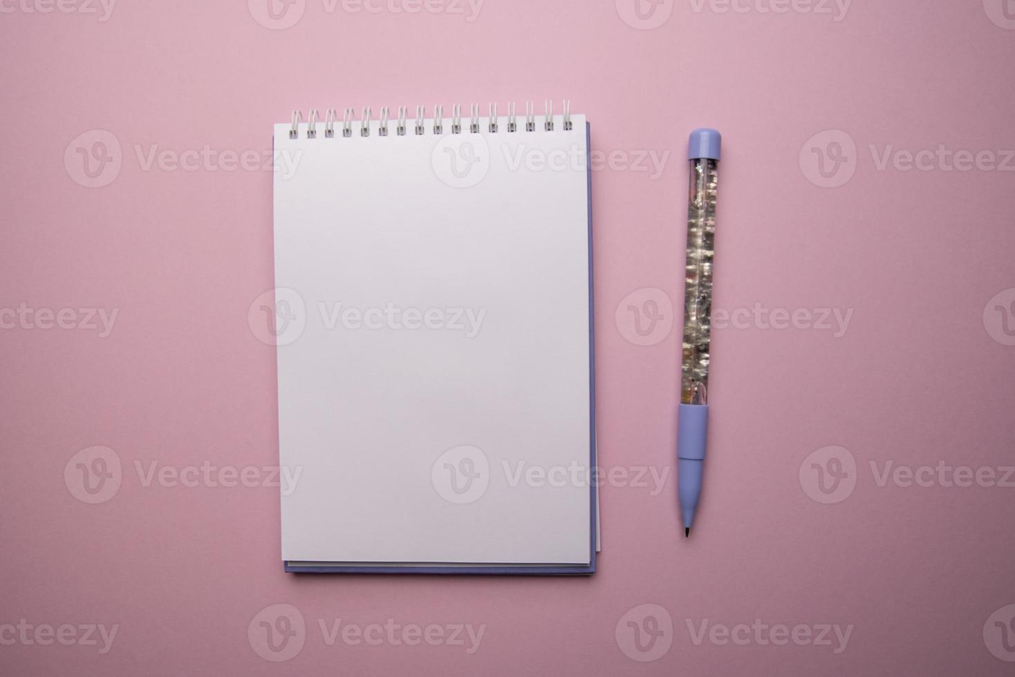Top view of open empty spiral notebook with pen on pink background photo